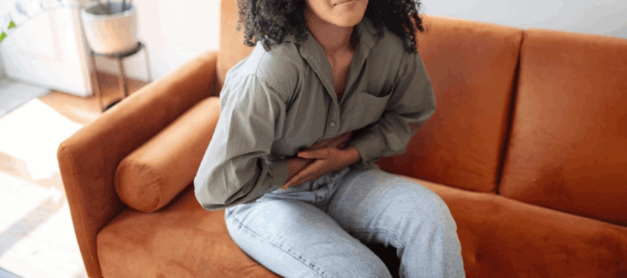 mulher com dor de barriga e mal-estar sentada no sof