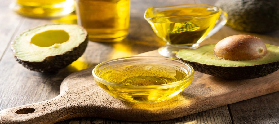 Tigela com azeite, fonte de gordura insaturada, rodeada por garrafas de azeite e metades de abacate em uma superf