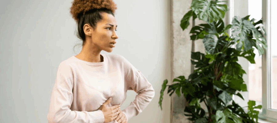 mulher com dor abdominal olhando pela janela e com uma das m
